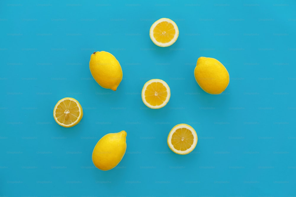 黄色いレモンと明るい青い紙にレモンのスライス、トレンディなフラットレイ。フルーツのモダンな画像、上面図。ジューシーな夏のビタミンとダイエットのコンセプト。ポップアートスタイル。クリエイティブミニマリズムパターン