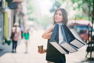 Portrait of woman holding paper bags and coffee on the street after shoping.