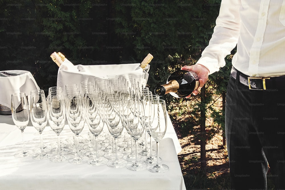 Kellner schenkt stilvolle Luxusgläser für Champagner auf einen Tisch für eine Feier und Cathering im Restaurant