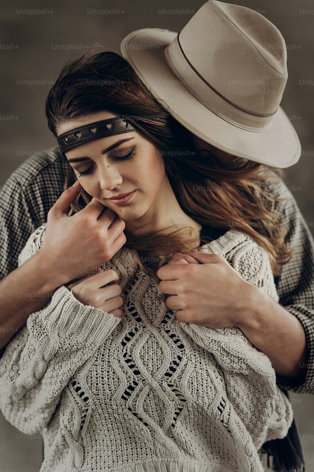 Hombre vaquero guapo con sombrero blanco tocando la mejilla de la hermosa mujer gitana boho con diadema de cuero, retrato de primer plano de la cara
