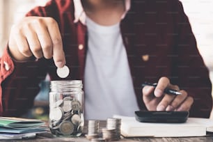 Man hand putting money (coin) in the glass jar during use calculator for calculate income or tax - Financial Business Concept