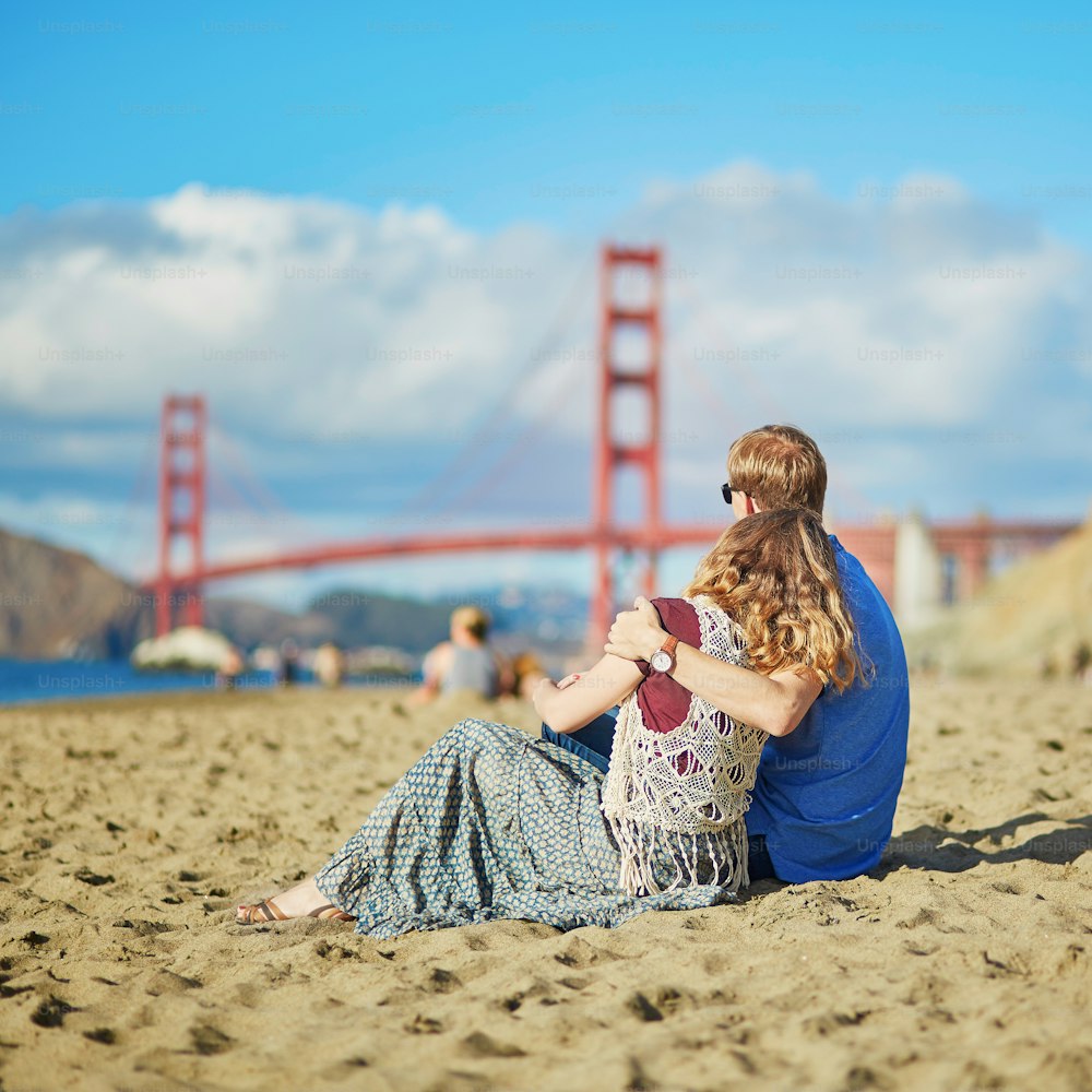 米国カリフォルニア州サンフランシスコのベイカービーチでデートをするロマンチックなカップル。背景にゴールデンゲートブリッジ