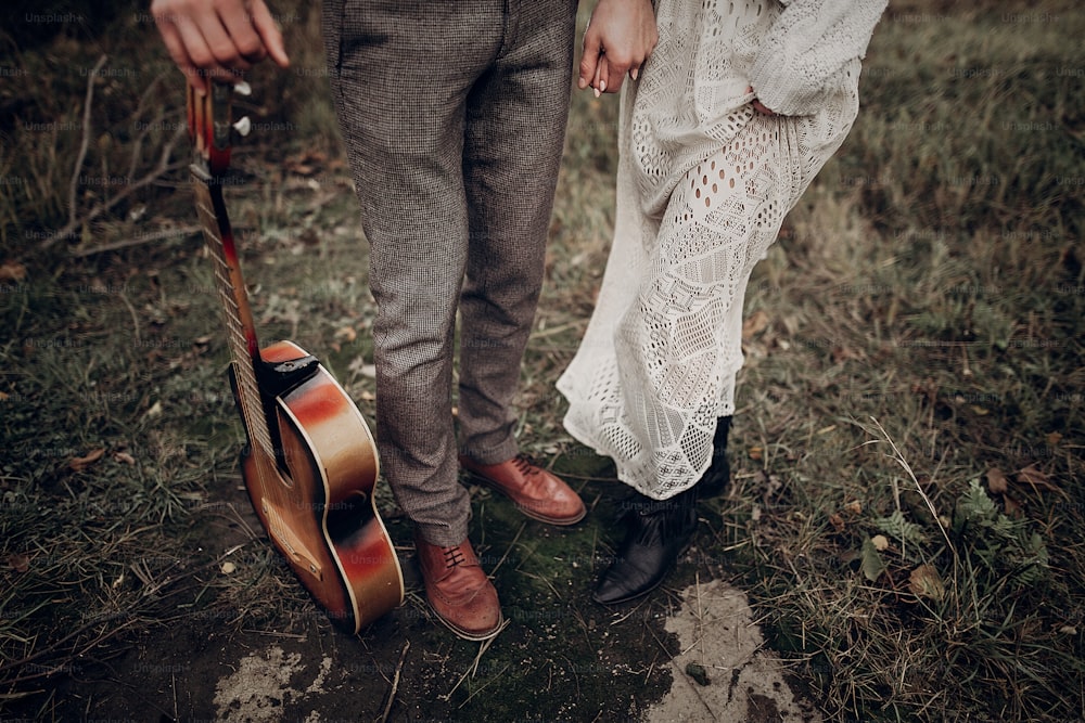 man with guitar holding hands with his boho gypsy woman closeup in windy field. atmospheric sensual moment. stylish hipster couple in fashionable look. rustic wedding concept