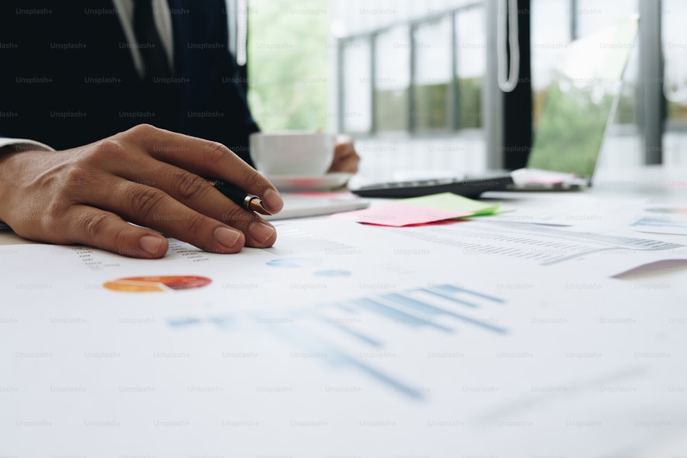 Data analyzing. Close up of business man adviser using pen pointing document report and discussing while hand holding a cup of coffee in his office