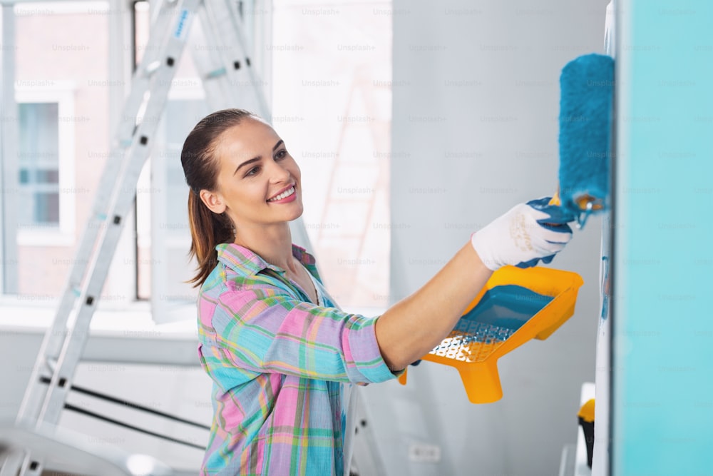 Interesante idea. Mujer delgada exuberante pintando la pared en color azul y usando guantes