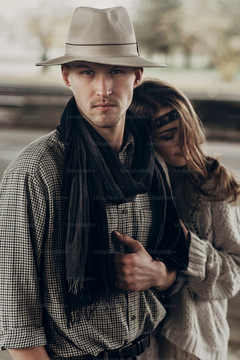 Homem cowboy bonito com um chapéu branco e lenço preto em uma camisa elegante sendo abraçado por uma bela mulher indie, olhar sedutor