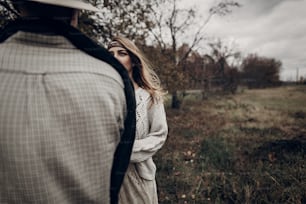 Stylish hipster man in cowboy shirt and hat looking at emotional gypsy hipster woman, autumn field background