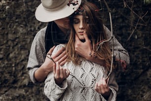 Homme romantique sensuel en chapeau de cow-boy étreignant une belle femme brune gitane par derrière, tandis qu’elle tient une branche d’arbre à baies en gros plan