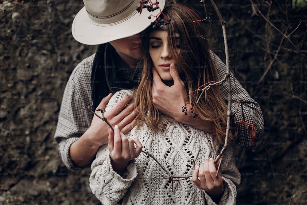 Sensual romantic man in cowboy hat hugging a beautiful gypsy brunette woman from behind, while she is holding a berry tree branch closeup