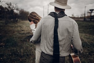 Stylish hipster man in cowboy shirt and hat holding emotional beautiful brunette woman, texas outdoors background