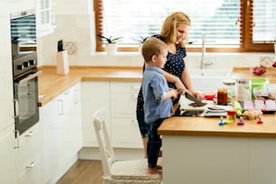 Smart cute child helping mother in kitchen preparing cookies