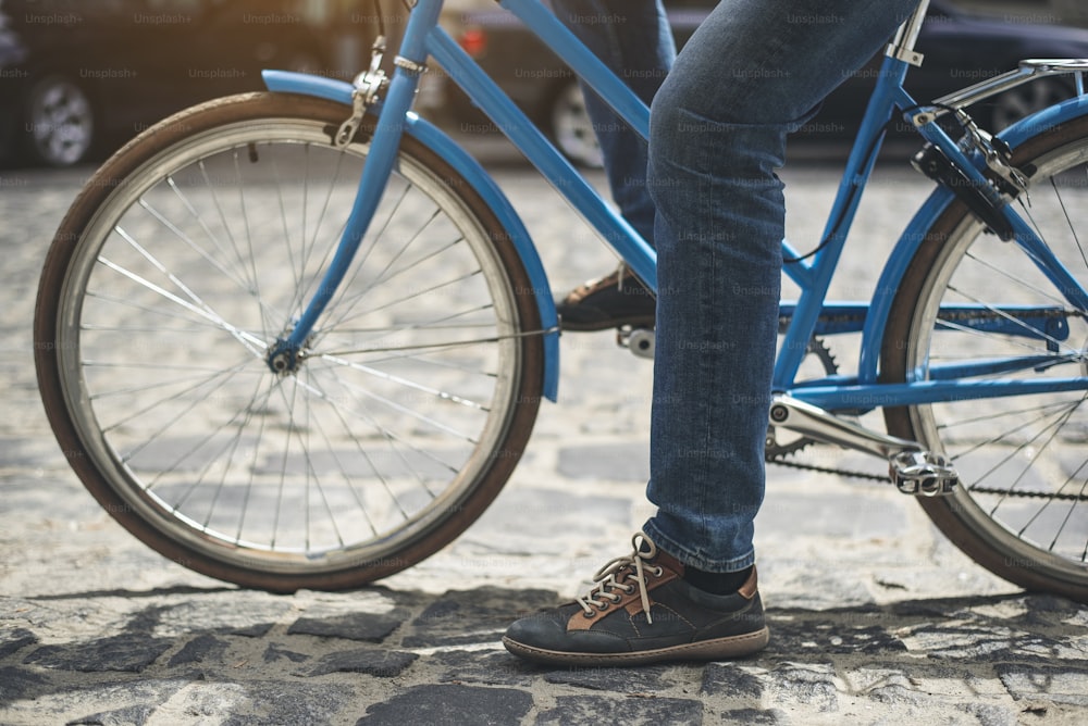 Conceito de estilo de vida ativo. Close up das pernas do homem começando a andar de bicicleta na estrada feita de pedra de pavimentação