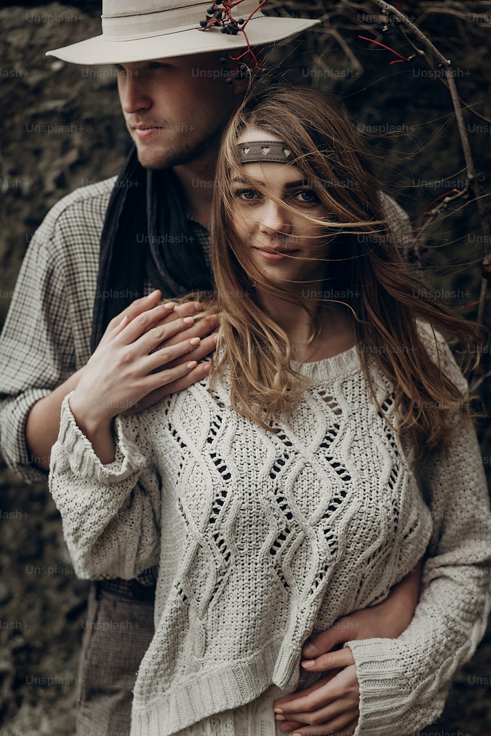 Beautiful brunette gypsy girl, hipster woman in boho white sweater holding hands with handsome man in cowboy hat, free couple outdoors