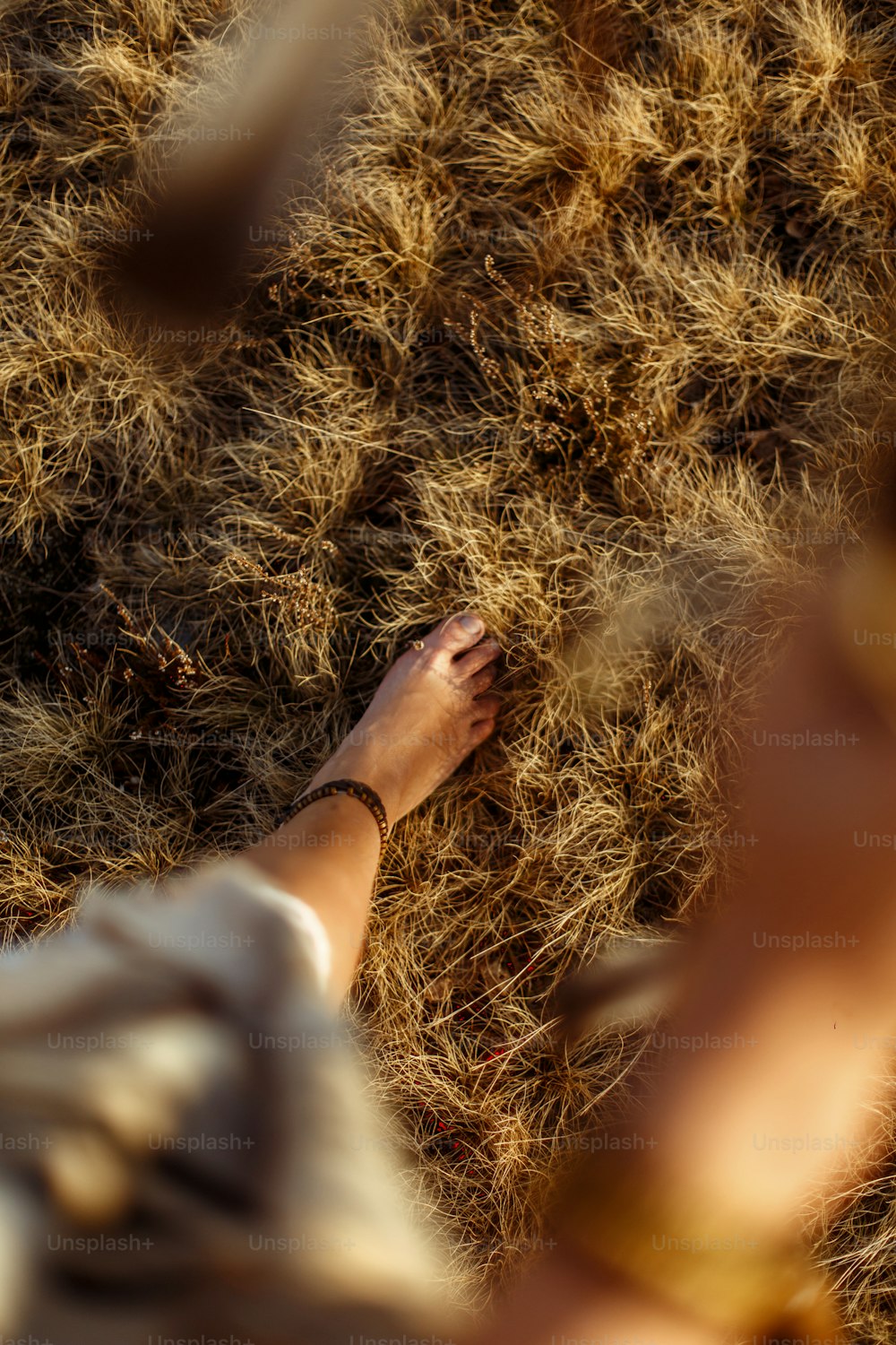 Frauenbeine im indianischen Boho-Kleid beim Wandern in windigen, sonnigen Abendbergen, Federn halten