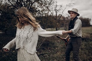 Couple hipster romantique, bel homme musicien avec guitare et femme gitane en pull bohème dansant dans le champ d’automne