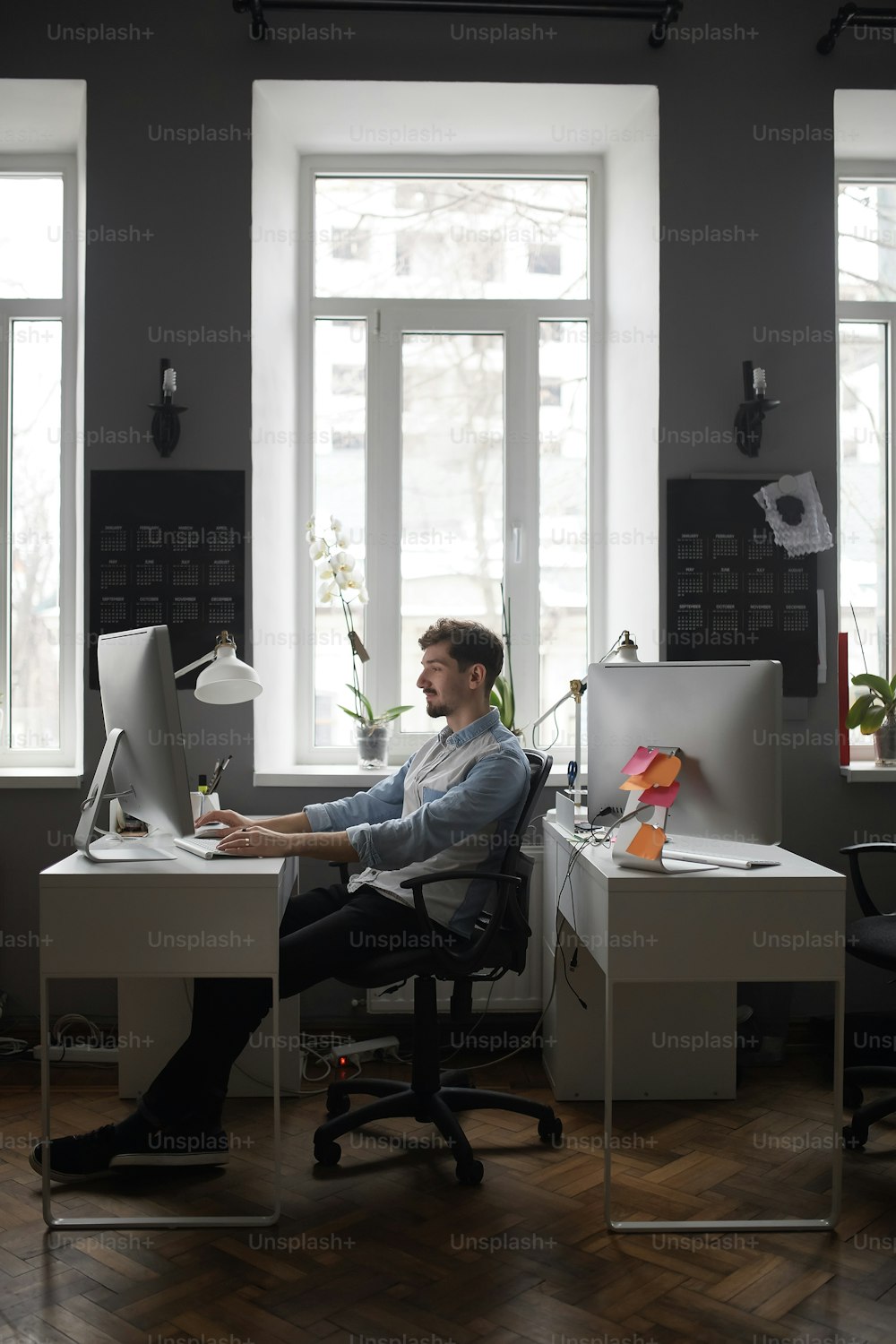 Vue grand angle d’un bureau d’études avec un beau jeune homme à des bureaux travaillant, tout en discutant dans une vidéoconférence avec des collègues, des clients.