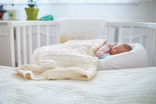 Newborn baby girl having a nap in co-sleeper crib attached to parents' bed