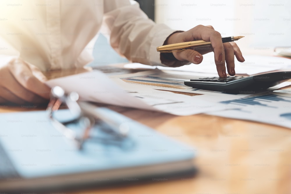 Close up Business woman using calculator and laptop for do math finance on wooden desk in office and business working background, tax, accounting, statistics and analytic research concept