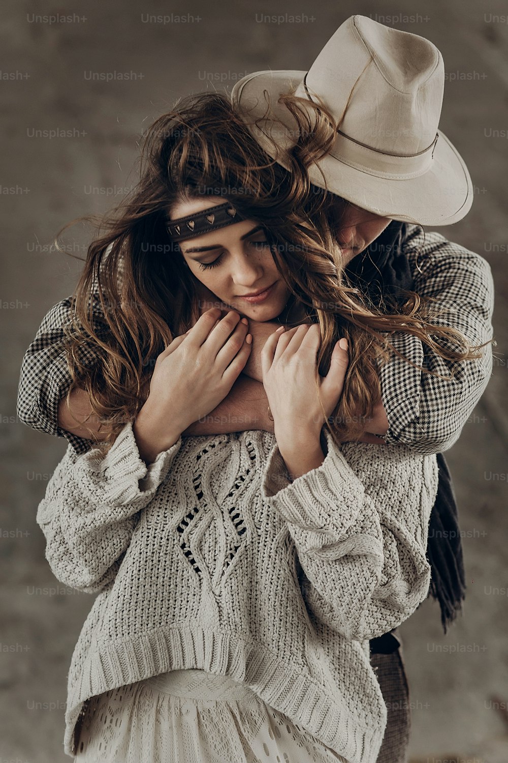 Strong cowboy man in white stylish hat hugging beautiful brunette hipster girl from behind