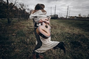 rustic wedding concept. man with guitar dancing with his boho gypsy woman  in windy field. stylish hipster couple hugging. atmospheric sensual moment. fashionable look.