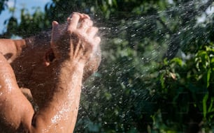 adult man takes a shower under a garden hose in a summer green garden. Picturesque summer courtyard