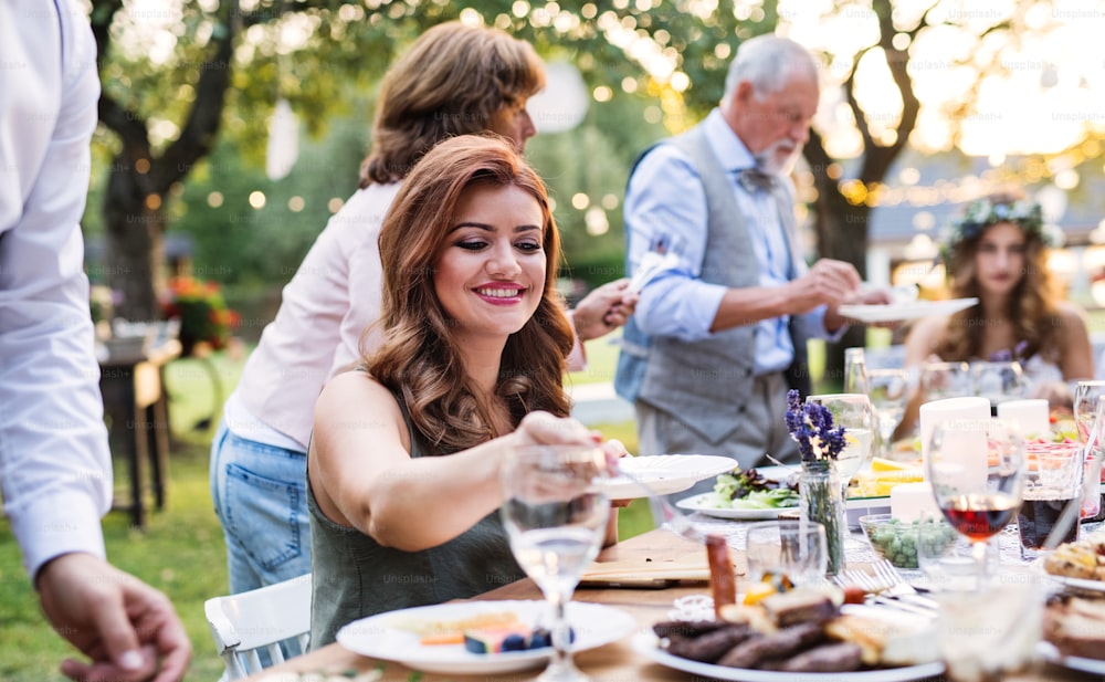 テーブルに座って、裏庭の外の結婚披露宴で食事をするゲスト。