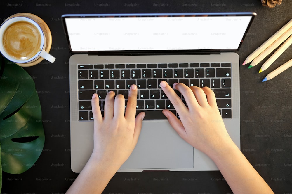 Draufsicht weibliche Hand tippenden Laptop. Weibliche Hände tippen auf einer Laptop-Tastatur mit Kaffeetasse auf dem dunklen Lederschreibtisch.