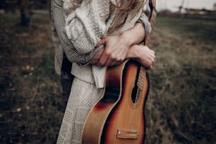 Hipster musician couple hugging in field, handsome man embracing gypsy woman in white dress, guitar closeup