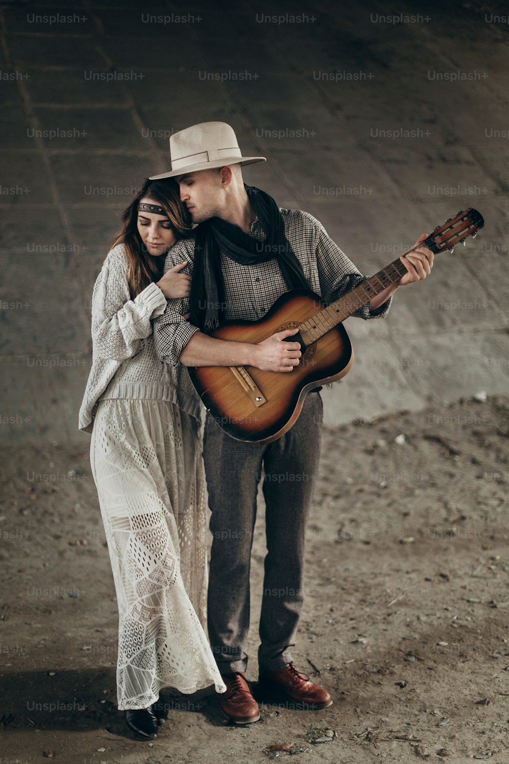 stylish hipster couple gently hugging. man in hat playing guitar for his boho woman in knitted sweater. atmospheric sensual moment. rustic fashionable look.