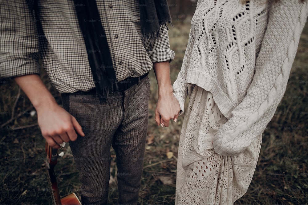 Sensual couple, gypsy woman in white boho dress holding hands with stylish musician man in texas field, closeup