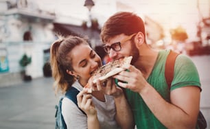 Positive happy students eating pizza on street