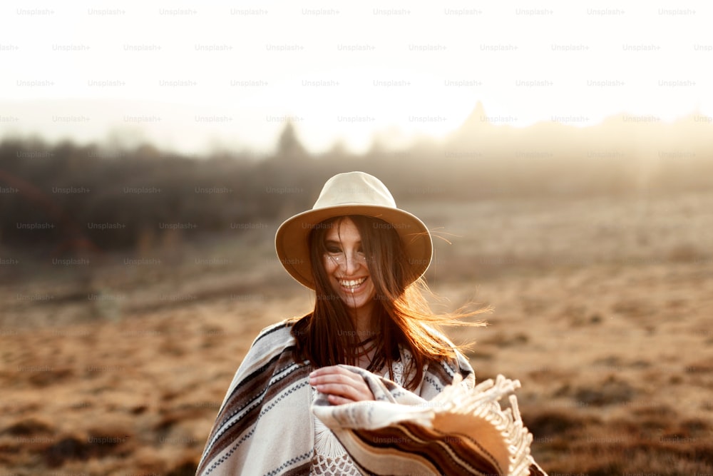 feliz boho mulher hipster, sorrindo ao pôr do sol nas montanhas, usando chapéu e poncho, emoções verdadeiras, espaço para texto