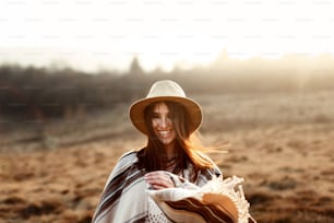 donna boho felice hipster, sorridente al tramonto in montagna, indossare cappello e poncho, emozioni vere, spazio per il testo
