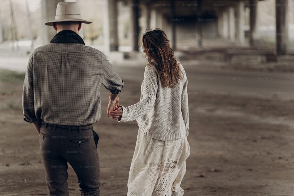 Handsome texas cowboy man in white hat holding hands with beautiful gypsy woman in white dress, couple walking in the city