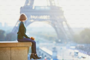 Beautiful young French woman with bunch of colorful autumn leaves near the Eiffel tower in Paris on a fall day