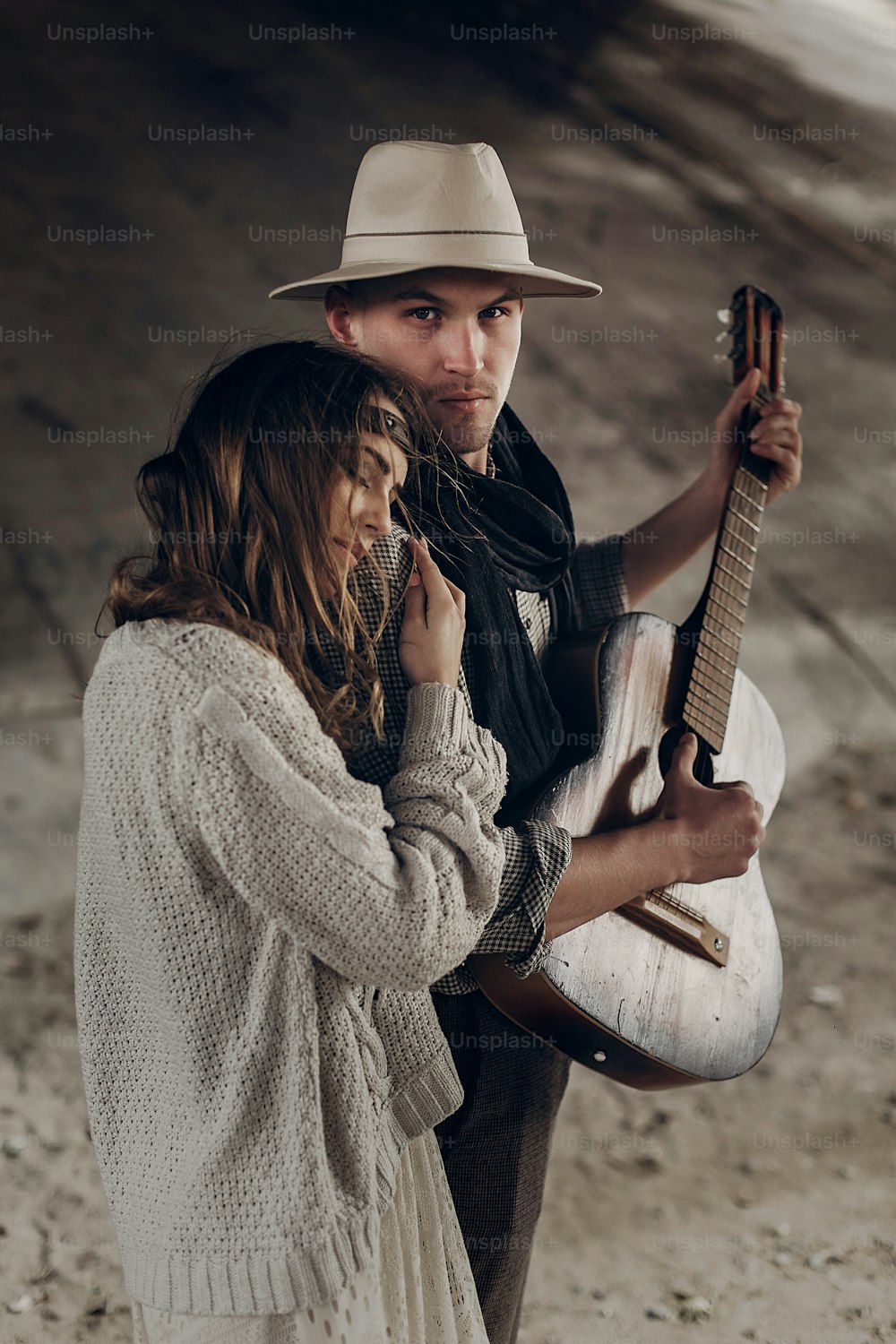 Handsome musician man with guitar and cowboy hat hug with sensual brunette hipster woman
