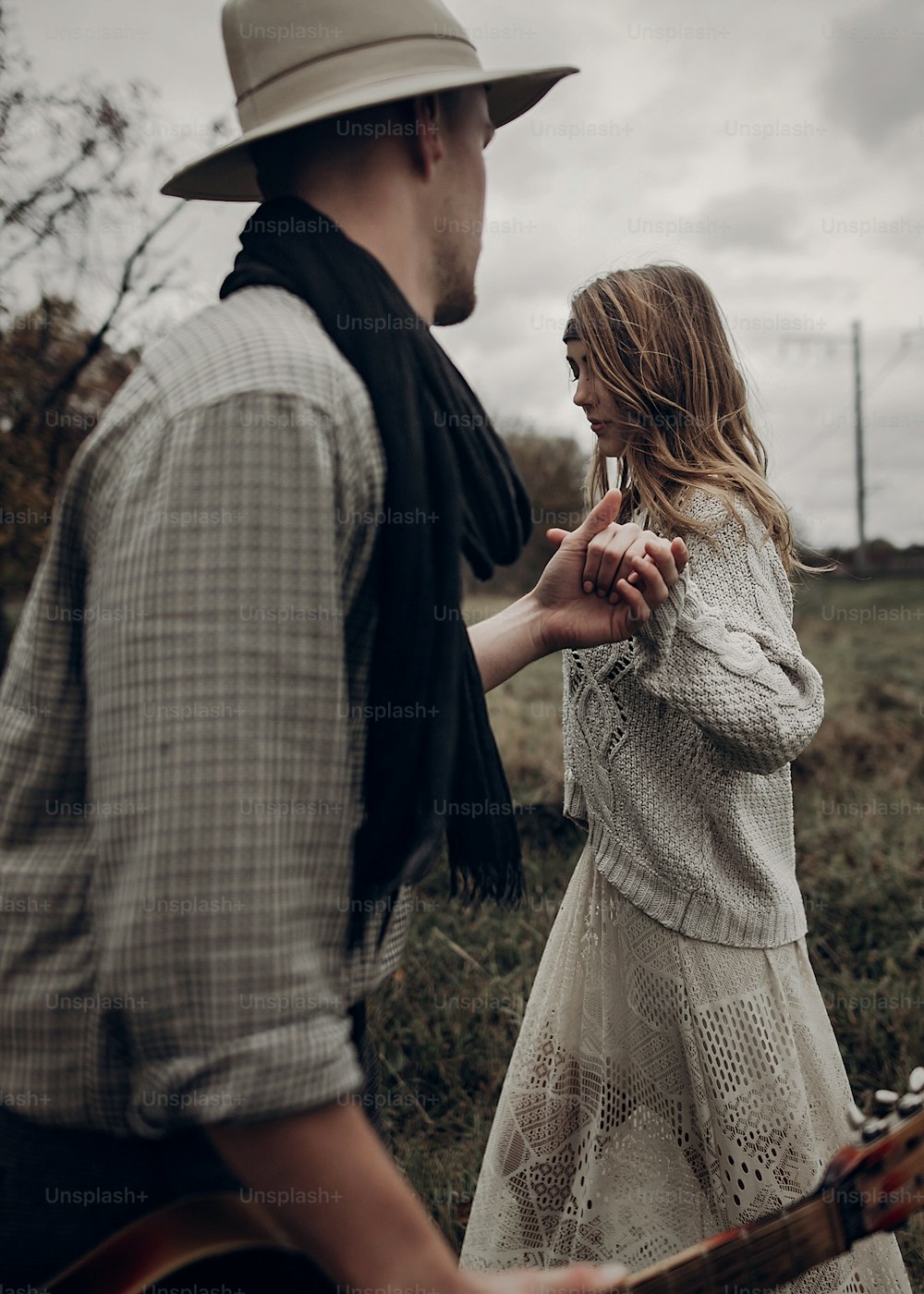 stylish hipster couple holding sensually hands. boho gypsy woman and man in hat embracing in windy field. atmospheric amazing moment. fashionable look. rustic wedding concept