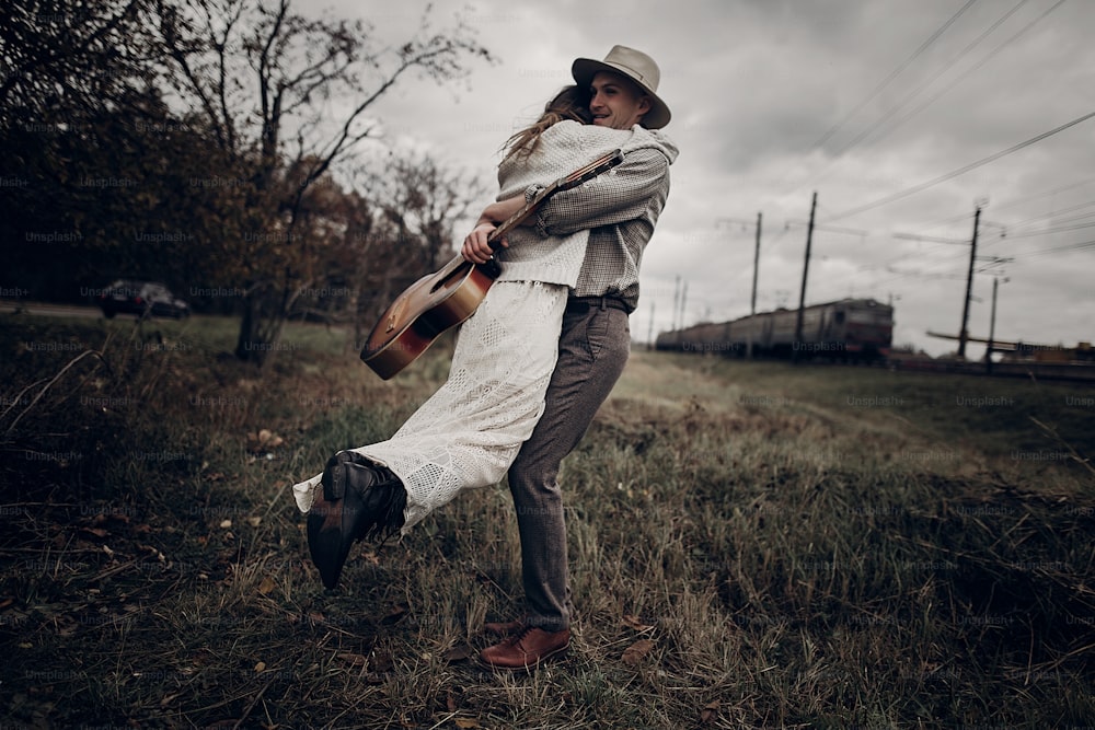 man with guitar dancing with his boho gypsy woman in windy field. stylish hipster couple hugging. atmospheric sensual moment. fashionable look.rustic wedding concept.