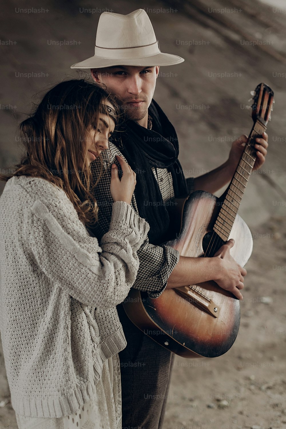 Handsome musician man with guitar and cowboy hat hug with sensual brunette hipster woman