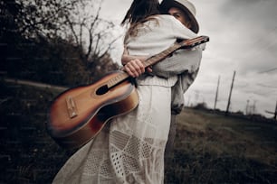 man with guitar dancing with his boho gypsy woman in windy field. stylish hipster couple hugging. atmospheric sensual moment. fashionable look.rustic wedding concept.