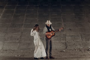 Mujer gitana con estilo en ropa boho bailando cerca de un hombre guapo, músico vaquero con guitarra