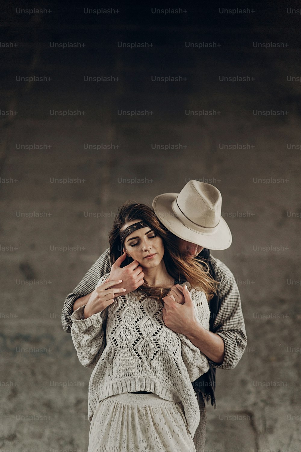 Handsome cowboy man in white hat touching cheek of beautiful boho gypsy woman with leather headband, posing outdoors