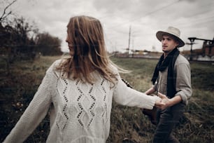 stylish hipster couple holding sensually hands. boho gypsy woman and man in hat embracing in windy field. atmospheric motion moment. fashionable look. rustic wedding concept