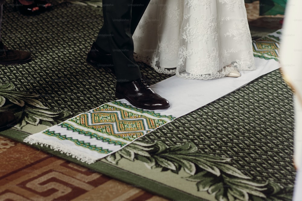 Cerimonia nuziale tradizionale slava, sposa e sposo alla moda che camminano sull'asciugamano bianco durante l'incoronazione, primo piano di nozze della chiesa cristiana