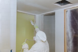 Man painting walls with white colour using spray paint gun hand the tool the spray of paint