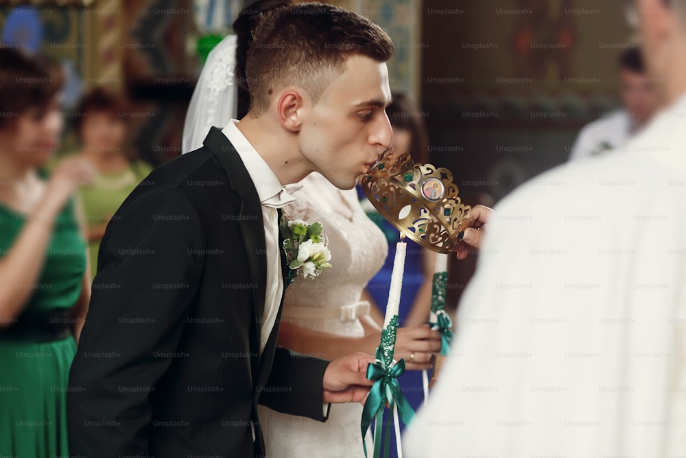 Couple spirituel heureux, marié élégant et belle mariée brune en robe blanche tenant des bougies lors de la cérémonie de mariage à l’église lors du couronnement de la couronne d’or