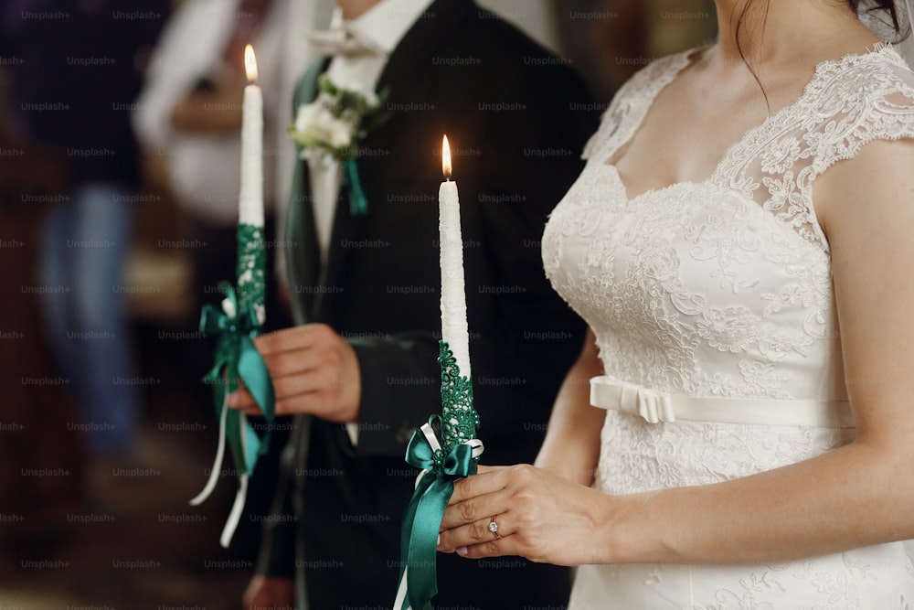 splendida sposa e sposo elegante che tengono candele alla cerimonia ufficiale di nozze nella vecchia chiesa. momento tradizionale