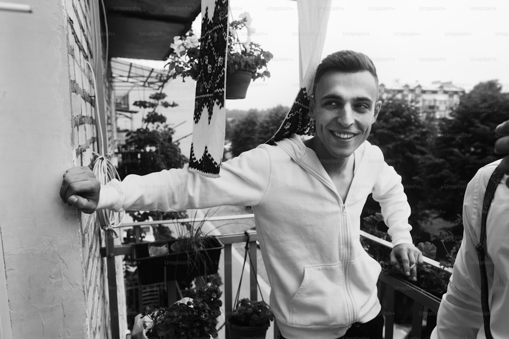Bel homme émotionnel en sweat-shirt blanc debout sur le balcon, marié souriant, matin avant le mariage