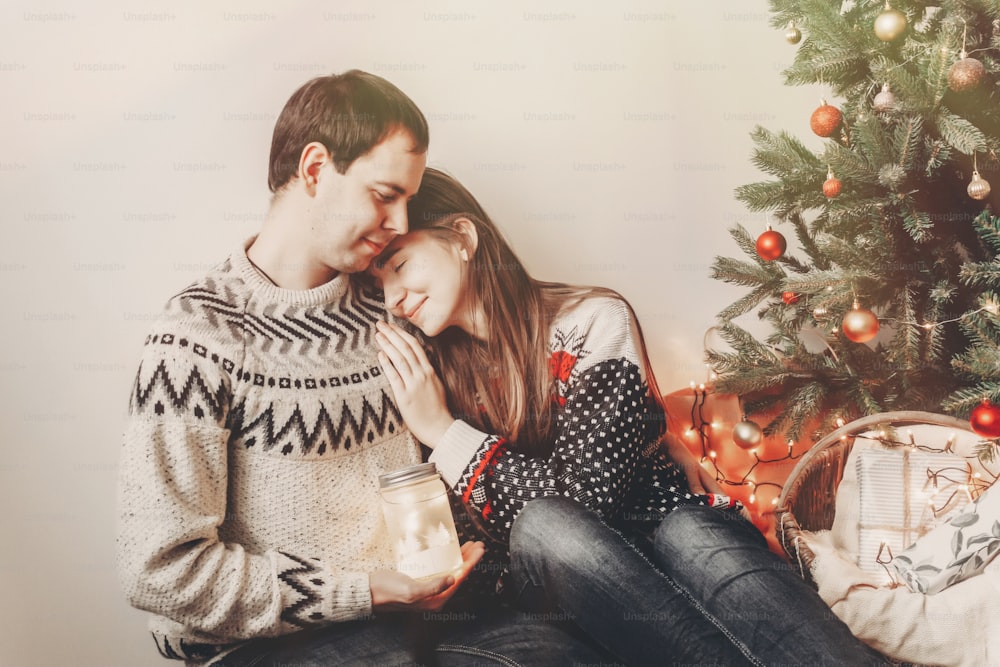 메리 크리스마스와 새해 복 많이 받으세요. 크리스마스 트리의 축제 방에서 랜턴 조명을 들고 스웨터를 입은 세련된 힙스터 가족. 즐거운 휴일 보내세요. 아늑한 가족의 순간