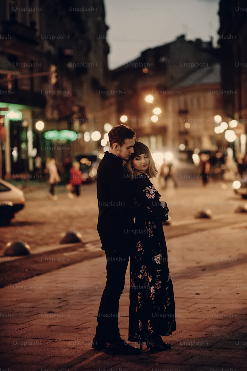 Romantic couple hugging in evening Paris street, handsome bearded man holding beautiful blonde woman in black floral dress outdoors, couple portrait, city lights in the background